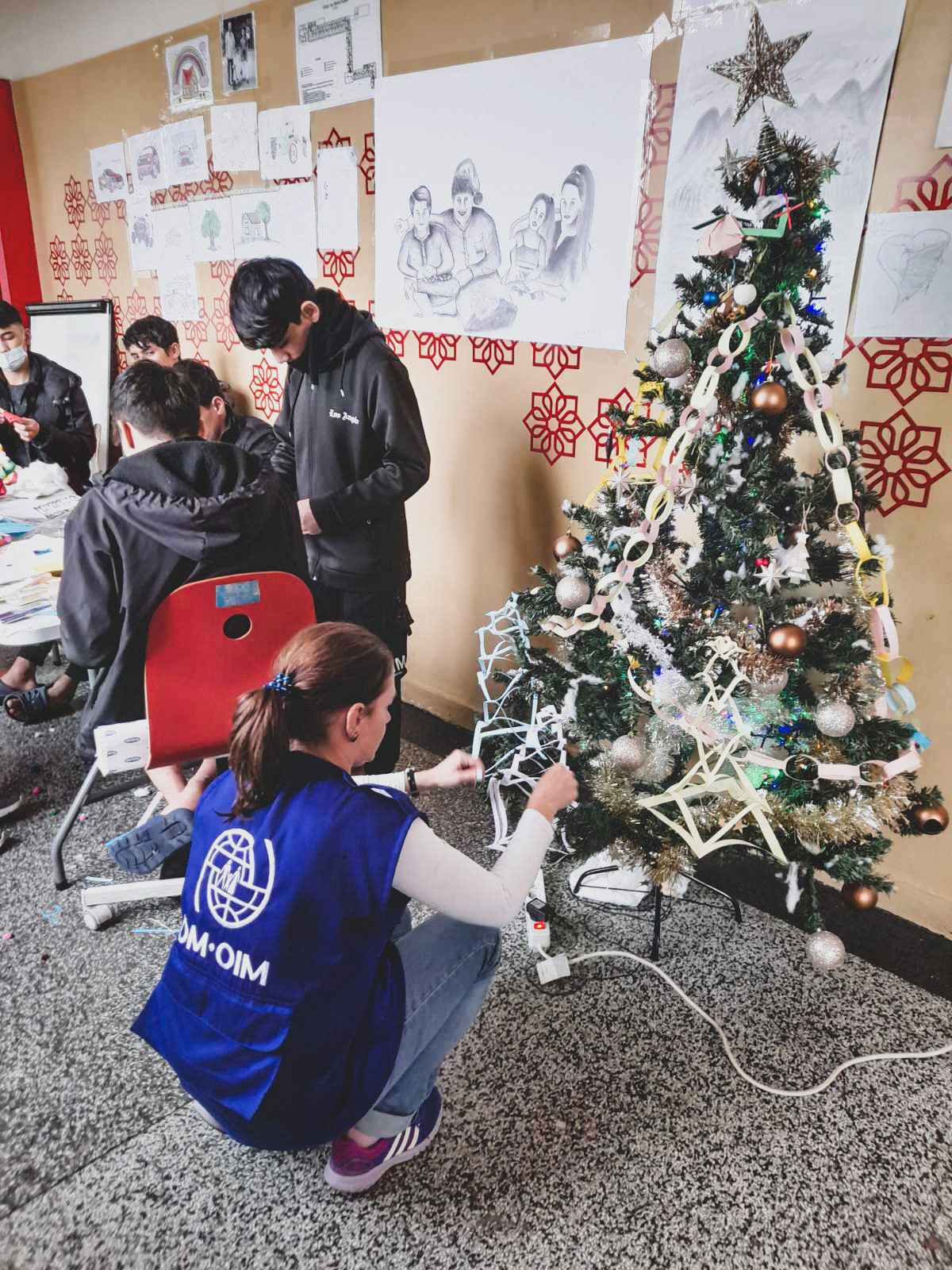 unaccompanied minors making Christmas decoration and an IOM team member